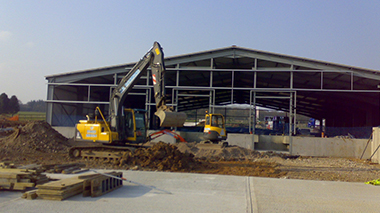 a digger take up the soil in front of a steel frame building 
