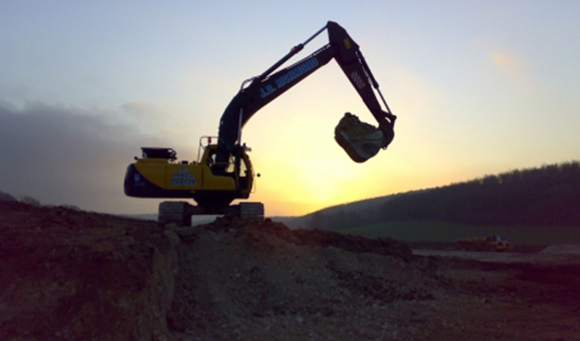 a digger on a hill with the sun setting behind it