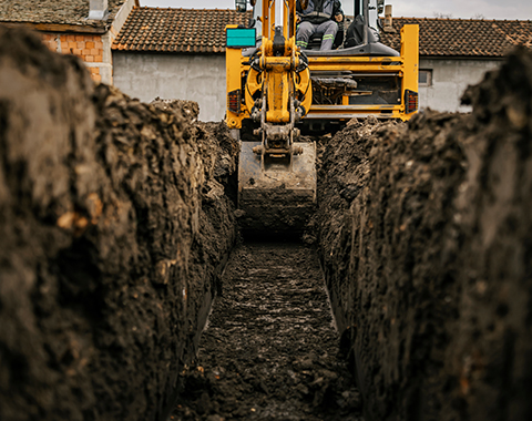 a yellow digger creating a trench in the ground 
